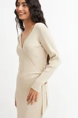 Vestido midi color crema, tejido en punto acanalado, con escote cruzado en V, mangas largas y lazo ajustable en la cintura.