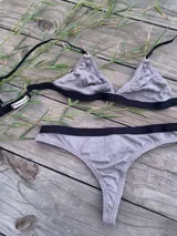Conjunto de lencería de color gris melange, compuesto por un bralette de copas triangulares y una bombacha colaless, ambos con detalles de elásticos anchos en color negro.