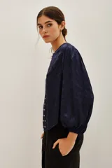 Camisa azul marino de corte holgado con mangas abullonadas, cuello redondo y abertura frontal decorada con tachas metálicas plateadas.