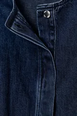 Chaqueta estilo bomber de denim azul oscuro, con cuello redondo, manga larga abullonada con puño elástico y bajo elástico. Presenta bolsillos delanteros de vivo y cierre frontal con botones ocultos.