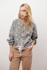 Bomber de tela liviana color beige con textura sutil, cierre frontal completo, mangas largas con puños elásticos y cordón ajustable en el ruedo.