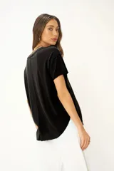 Camiseta de cuello en V con hombros caídos, dobladillo curvo y ajuste holgado. Presenta bordes sin rematar y costuras expuestas, confeccionada en una tela suave y texturizada.