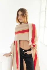 Ruana artesanal de tejido de punto, color beige con franjas horizontales gruesas rojas y finas amarillas. Posee flecos en el borde inferior.