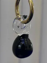Aros de argolla dorada con dije colgante compuesto por una pieza de vidrio transparente en forma de espiral y una pieza de vidrio negro en forma de gota.