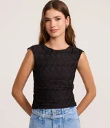 Blusa sin mangas de color negro, confeccionada en poliéster con textura en relieve, cuello redondo y corte al cuerpo.