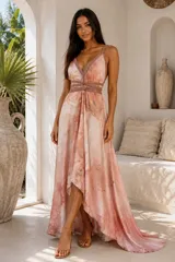 Vestido largo asimétrico de seda de India con estampado abstracto en tonos rosados y destellos dorados. Presenta escote en V profundo con tiras tejidas decorativas que contornean el busto y la cintura, tirantes finos y falda fluida con corte más corto en la parte delantera.
