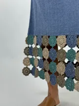 Vestido midi de tejido ligero color beige, con cuello en V, mangas cortas y ruedo decorado con aplicaciones de crochet en tonos tierra y rosado.