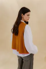 Chaleco tejido color mostaza con bordado artesanal en forma de V al tono. Tiene cuello redondo y sisas con sobretono.