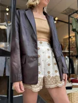 Blazer de cuero sintético en color marrón oscuro, con cierre frontal de dos botones y solapas clásicas.