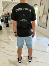 Remera negra de corte clásico con estampado gráfico en la espalda con el texto "Underwave Brand. Surfing Lifestyle Since 2014" en colores verde claro y blanco.