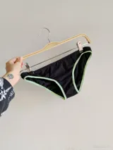 Conjunto de dos piezas compuesto por un top y una bombacha. El top es negro con ribetes en color verde claro y tirantes fucsias. La bombacha es negra con detalles en verde claro.