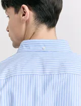 Camisa de corte clásico confeccionada en tejido oxford, con diseño de rayas verticales en tonos azul y blanco. Presenta cuello abotonado, cierre frontal con botones y bolsillo en el pecho con detalle de etiqueta bordada.