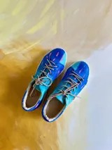 Sneakers de cuero vacuno con diseño artístico pintado a mano en tonos azul, turquesa y detalles en rosado, con cordones beige y suela de goma.