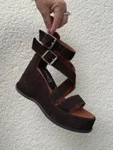 Sandalias de cuero marrón con acabado en gamuza, taco de 8 cm y plataforma forrada. Diseño con doble tira ajustable con hebillas metálicas y cierre trasero.