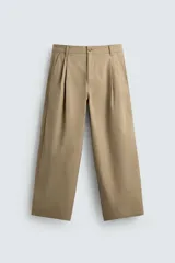 Pantalón chino de corte wide fit confeccionado en tejido de algodón. Presenta pliegues frontales, bolsillos laterales y bolsillos traseros de vivo, con cierre frontal de cremallera y botón.