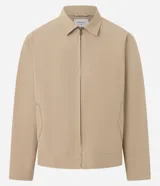 Campera de sarga color beige con cuello inglés, cierre frontal de cremallera, mangas largas y bolsillos laterales. Diseño minimalista y versátil con forro interior.