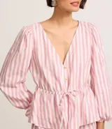 Blusa de tricolina con estampado de rayas verticales en color blanco y rosado. Presenta cuello en V, cierre frontal con botones, mangas 3/4 abullonadas y un lazo ajustable en la cintura.