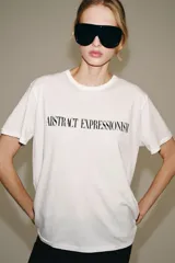 Camiseta oversize blanca de manga corta y cuello redondo, confeccionada en hilatura de algodón con detalle de texto estampado en contraste en el pecho.
