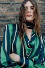 Camisa de manga larga con escote fluido tipo pañuelo, hombreras y puños abotonados. Presenta un diseño de rayas verticales en tonos verdes y amarillos.