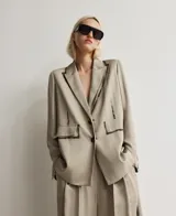 Blazer recto color topo (beige grisáceo) de viscosa, con solapa y cierre de dos botones. Presenta un diseño artístico con trazos oscuros simulando pintura en la solapa, costuras de la manga y un bolsillo de vivo con solapa en el lado derecho, mientras que el bolsillo izquierdo es pintado.