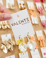 Aros de argolla dorada con dije colgante en forma de pétalos de flor en color blanco nacarado.