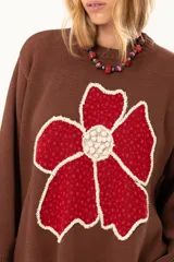 Buzo de punto color chocolate con diseño de flor grande en el frente en tonos rojos y centro texturizado en color crema. Presenta cuello redondo, mangas largas y puños y ruedo acanalados.