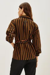 Saco tipo camisa de algodón con rayas verticales marrones y negras. Presenta bordados de cuentas en tonos tierra en el hombro izquierdo y se ajusta a la cintura con un lazo de viscosa estampado en tonos naranjas y negros.