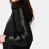 Hoodie oversize negro con capucha y bolsillo canguro frontal, con estampa gris de la marca EM ESTUDIOS en el pecho.