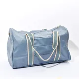 Bolso tipo duffel color celeste con textura símil cuero, doble asa corta de tela con rayas blancas y verde agua, cierre superior con cremallera y bolsillo interno.
