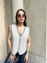 Chaleco tejido de punto color beige con corte sastrero, abotonadura frontal y detalle de bordado a mano en contraste a lo largo de los bordes.