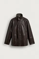 Cazadora de corte relaxed fit confeccionada en tejido efecto piel de color marrón. Cuenta con cuello subido forrado en su interior con tejido de cuadros, manga larga, bolsillos de vivo en la cadera y un bolsillo interior. El cierre frontal es con cremallera oculta por una solapa con botones a presión.