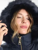 Campera puffer larga de color azul marino con capucha desmontable con borde de piel sintética. Cuenta con cierre frontal metálico dorado con logo grabado y bolsillos laterales con cierre.