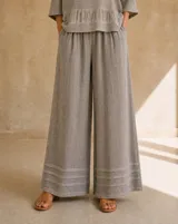 Pantalón palazzo de lino color gris, de corte ancho y relajado, con cintura elástica fruncida y detalles de pespuntes horizontales en el ruedo.