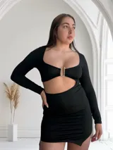 Minivestido negro de mangas largas, escote cuadrado con abertura en el abdomen y detalle de hebilla metálica. Falda ajustada con frunces laterales.