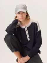 Buzo de manga larga con diseño de bloques de color. El cuerpo principal es azul marino liso, mientras que los hombros y la tapeta del cuello son de tejido texturizado color beige claro. Presenta costuras expuestas en contraste y un cuello redondo con tapeta de botones.