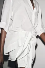 Camisa de color mostaza, con cuello solapa, manga corta y bajo recto. Cierre frontal con botones.