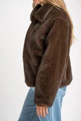 Abrigo de piel sintética en color marrón, con cuello clásico, cierre frontal con cremallera y mangas largas.