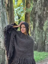 Poncho de lana merino color marrón oscuro, con diseño sin cuello, textura tejida y flecos largos en el ruedo.