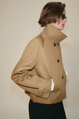 Chaqueta corta de cuello subido y manga larga con trabilla y botón. Cuenta con bolsillos de vivo en el delantero y cierre frontal con botones.