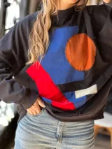 Buzo oversize negro con diseño artesanal de figuras geométricas aplicadas en tela de colores azul, naranja, rojo y blanco.