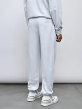 Pantalón jogger de felpa sin frisa, color gris claro melange, con logo bordado de Umbro en azul oscuro en el muslo izquierdo y puños elásticos en los tobillos.