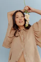 Camisa de lino color tostado, con cuello camisero y cierre frontal de botones. Se caracteriza por sus mangas cortas amplias y voluminosas que aportan un diseño fresco y liviano.