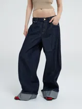 Pantalón de jean azul oscuro, de corte ancho y tiro medio, con dobladillo ancho en el bajo que deja ver el revés de la tela.