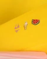 Neceser rectangular de tela color ladrillo con cierre superior y tres bordados pequeños: una hoja de arce, una taza de té y un croissant.