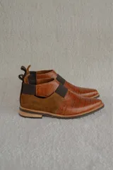 Zapato tipo botineta de cuero color bordó con textura grabada, diseño de punta fina y detalles de elásticos laterales en color negro.