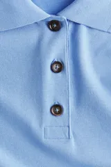 Remera polo de piqué de algodón en color celeste, con cuello acanalado, tapeta de tres botones, mangas al codo y hombros caídos. Presenta un corte holgado con bajo recto y aberturas laterales.