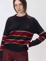 Sweater clásico de punto cable con cuello redondo a la base, mangas largas y fit al cuerpo. De color marrón con franjas horizontales violetas y amarillas, cuenta con el cuello, puños y ruedo acanalados, además de un pequeño logo bordado en el pecho.