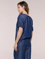 Blusa de calce relajado de lyocell en tono azul denim, con cuello a la base y cierre frontal de botones metálicos. Tiene mangas cortas abullonadas con puños elásticos.