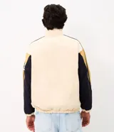Campera de sarga de algodón marca Blue Steel, con diseño de bloques de color en tonos beige, negro y mostaza. Presenta cuello alto, cierre frontal con botones a presión y solapa, bolsillos laterales y detalles de parches bordados con temática outdoor en el pecho y la manga.