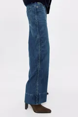 Jean de corte wide leg tiro alto, confeccionado en denim azul con efecto desgastado. Presenta diseño de cinco bolsillos, detalles trenzados a los lados y dobladillo ancho pespunteado.